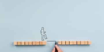 Male hand drawing a bridge between two rows of wooden blocks for a silhouetted man to walk across. Over blue background with plenty of copy space.