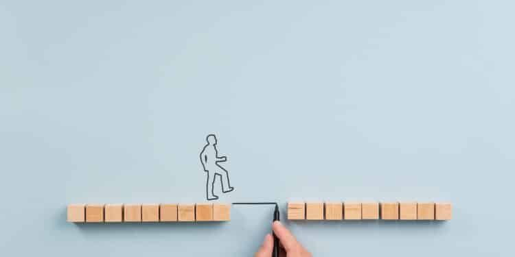 Male hand drawing a bridge between two rows of wooden blocks for a silhouetted man to walk across. Over blue background with plenty of copy space.