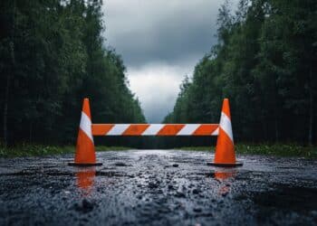 Wet road with traffic cones and road closed barricade during rainy weather conditions.